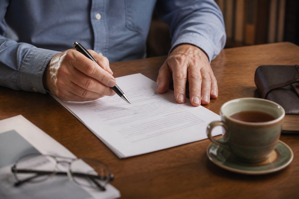 A close-up of a person's hands reviewing a legal document at a wooden desk, with a pen and a cup of tea nearby, conveying a calm and considered atmosphere