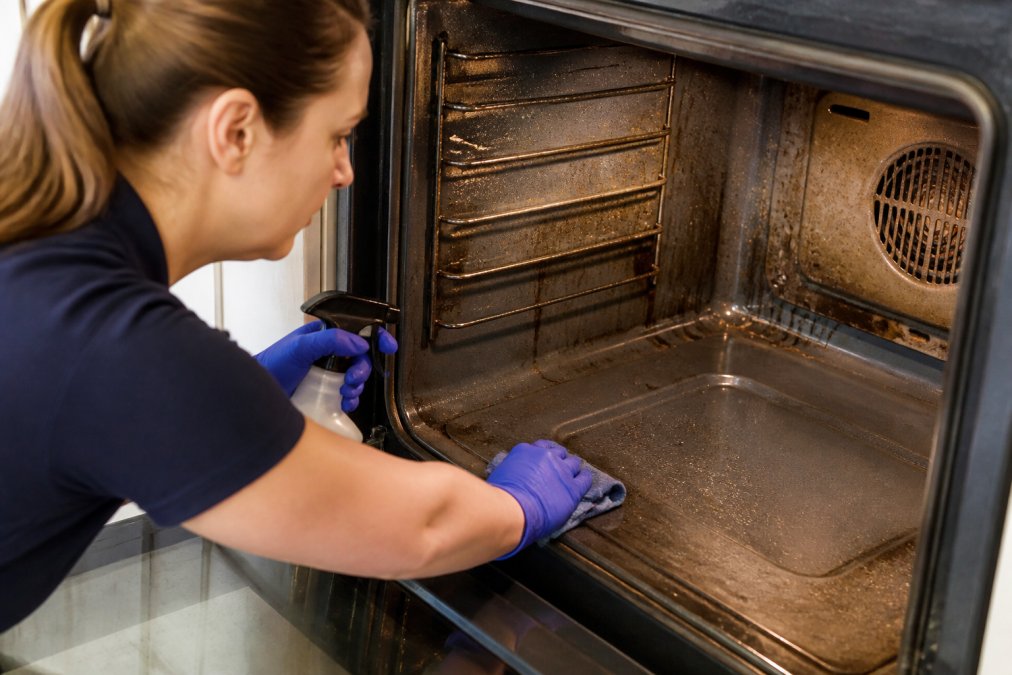 Professional demonstrating careful degreasing of oven interior using cloth and specialized cleaner, showing residue removal on stainless steel surfaces