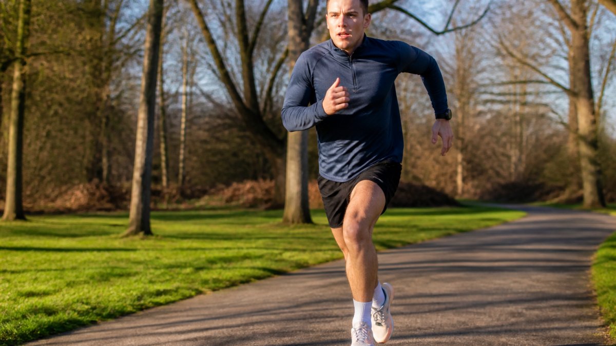 Runner in outdoor park setting, mid-stride during intense interval effort, showing focused expression and dynamic running form with natural morning light