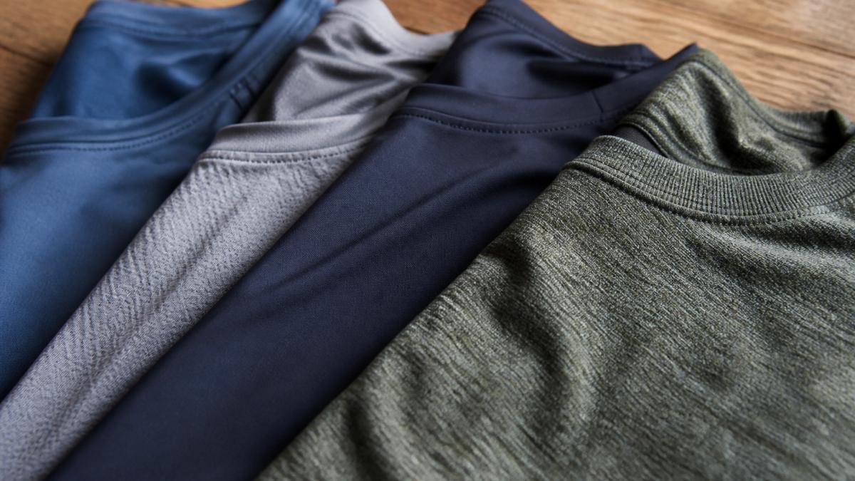 Close-up of folded athletic garments in different synthetic and natural fabrics showing texture variation between polyester's smooth sheen, nylon's slight luster, and merino wool's natural crimp structure