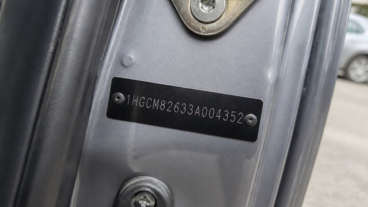 Close-up of a vehicle's VIN plate on the driver's side door jamb, showing the 17-character identification number clearly visible under natural daylight