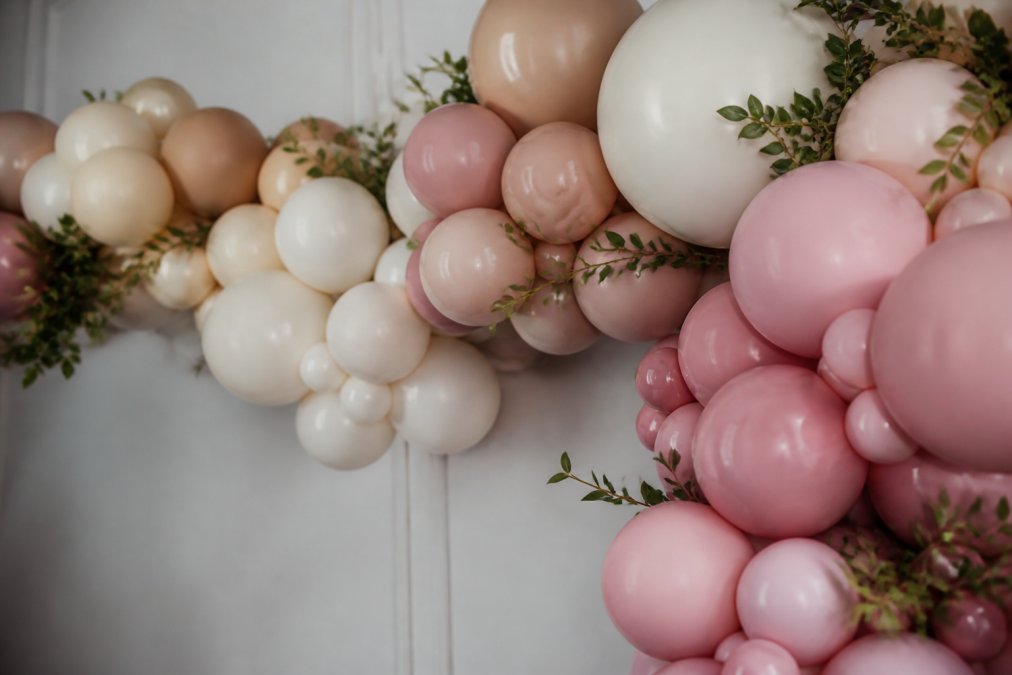 Close-up of an organic balloon garland installation showing asymmetrical arrangement of latex balloons in varying sizes and colors with natural flowing movement, demonstrating whimsical texture and visual balance against a neutral wall