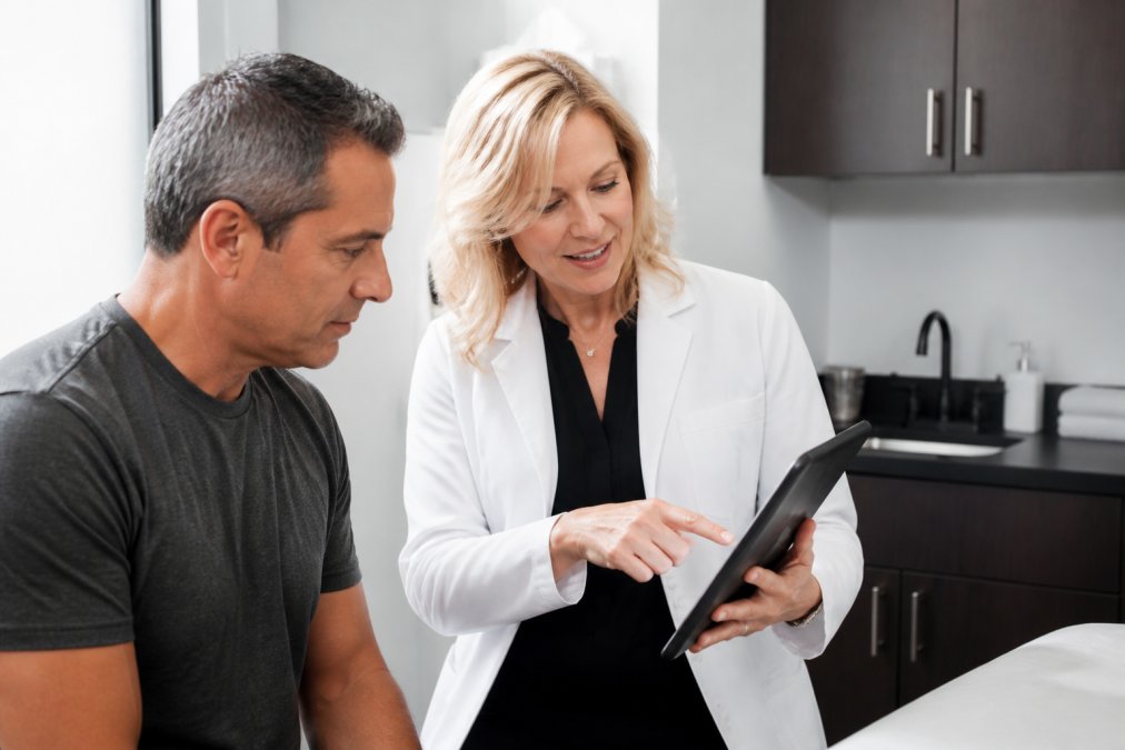 Healthcare provider explaining a peptide therapy plan to a patient in a modern clinic using a tablet with charts