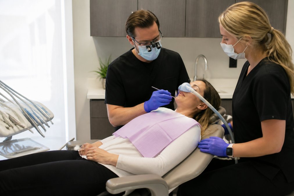 Calm patient wearing a nasal mask for sleep dentistry in a modern, spa-like dental treatment room with staff