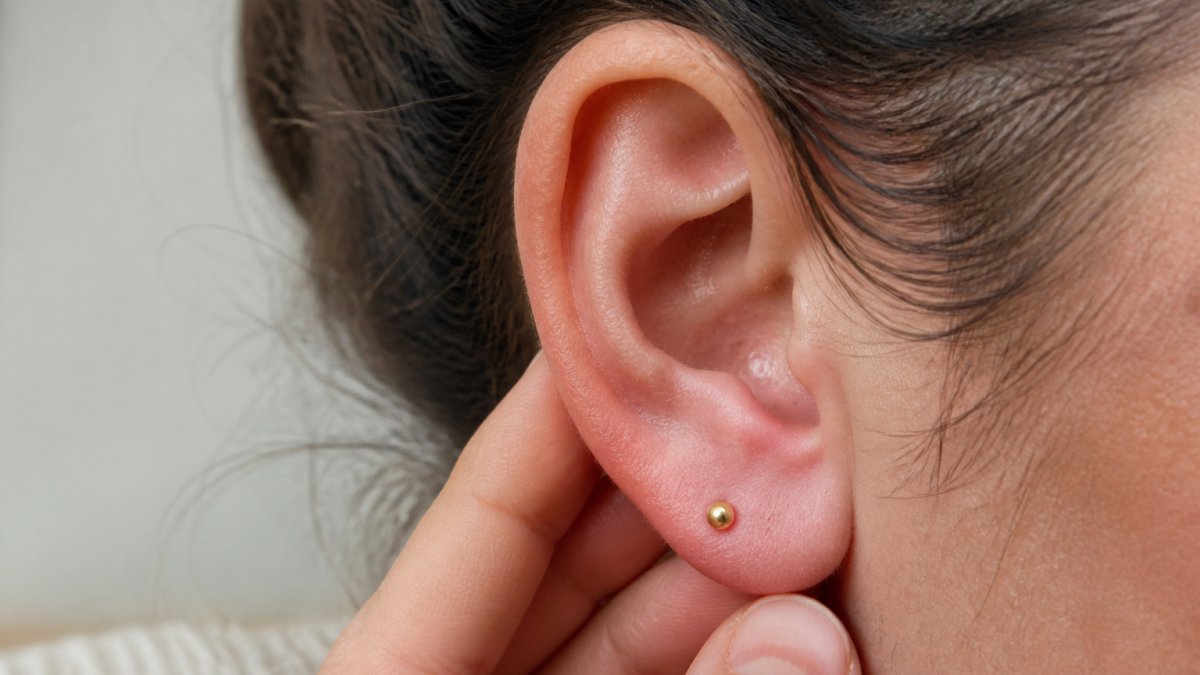 Close-up of a person's ear showing a healed piercing with a 14k gold piece, examining the area for any signs of irritation or sensitivity