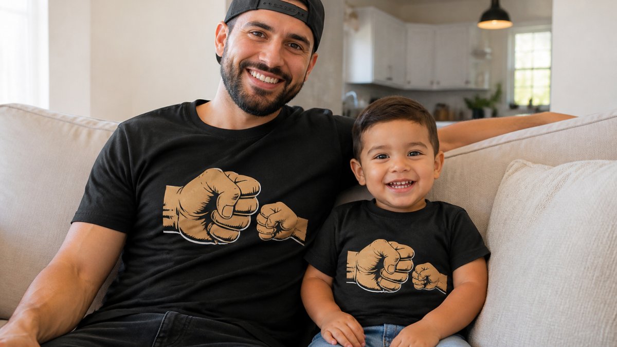 A smiling father and his young child sitting on a couch while wearing matching graphic cotton t-shirts