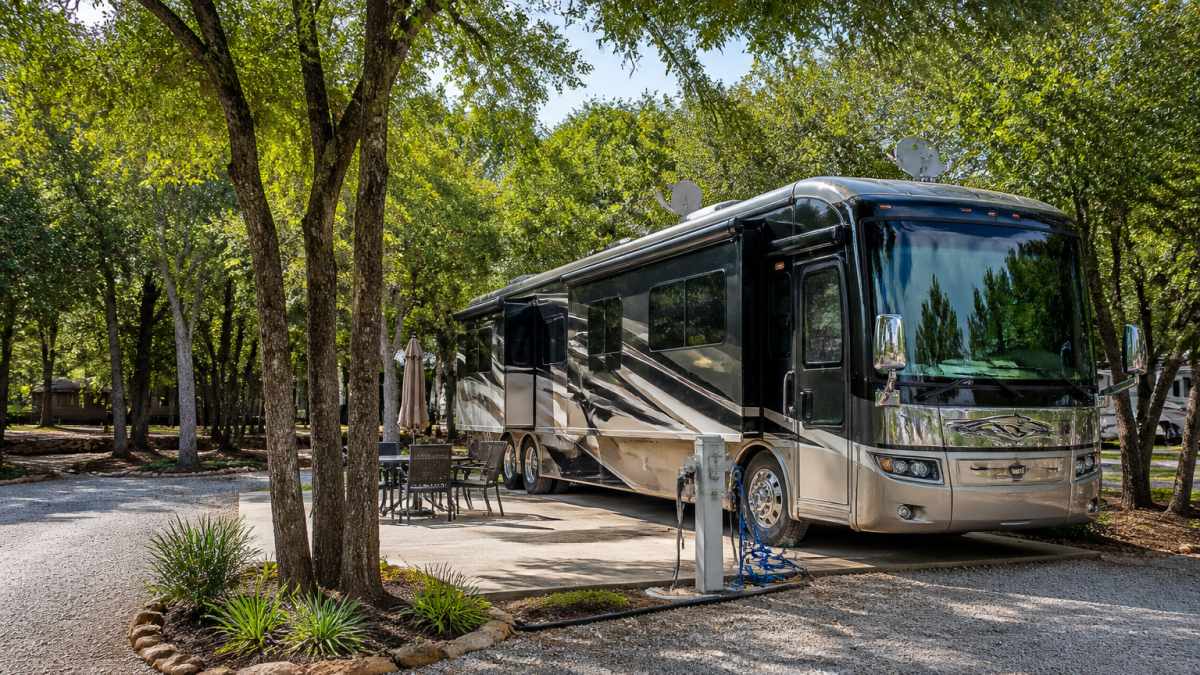 A peaceful wooded RV resort with shaded full-hookup sites, level concrete pads, and a well-maintained RV parked with visible electrical and water connections, surrounded by native Texas trees and natural landscaping