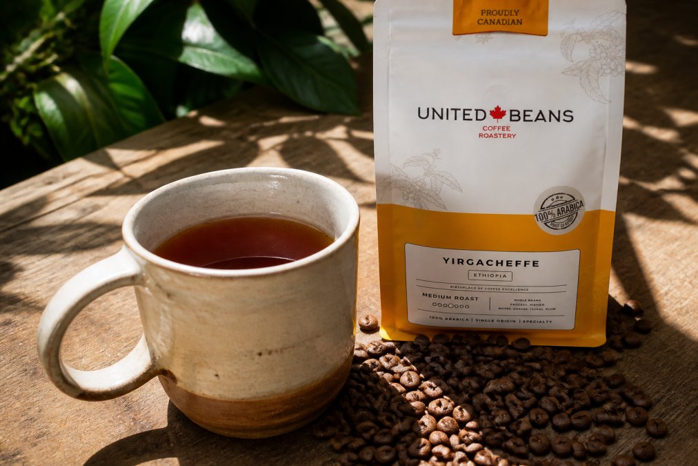 Close-up of a freshly brewed cup of light roast Ethiopian Yirgacheffe coffee showing its bright amber color, with coffee beans and a ceramic mug on a natural wood surface