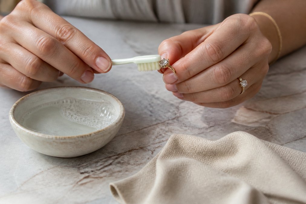 Woman cleaning an antique ring with vintage diamonds using a soft brush and soapy water on a marble countertop