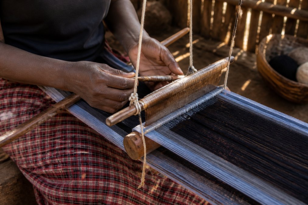 Close-up of an artisan's hands working a traditional backstrap loom, with natural fibers and wooden tools visible in a sunlit workshop