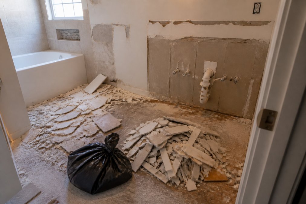 Bathroom undergoing renovation with removed vanity, scattered tile debris, drywall fragments, and demolition waste on the floor showing typical debris from a small remodel project