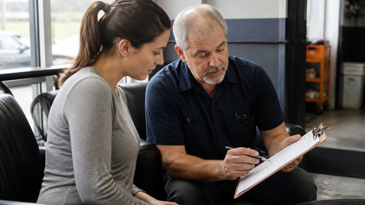 A customer and an ASE-certified mechanic reviewing a written estimate on a clipboard in a clean, well-lit auto repair shop waiting area