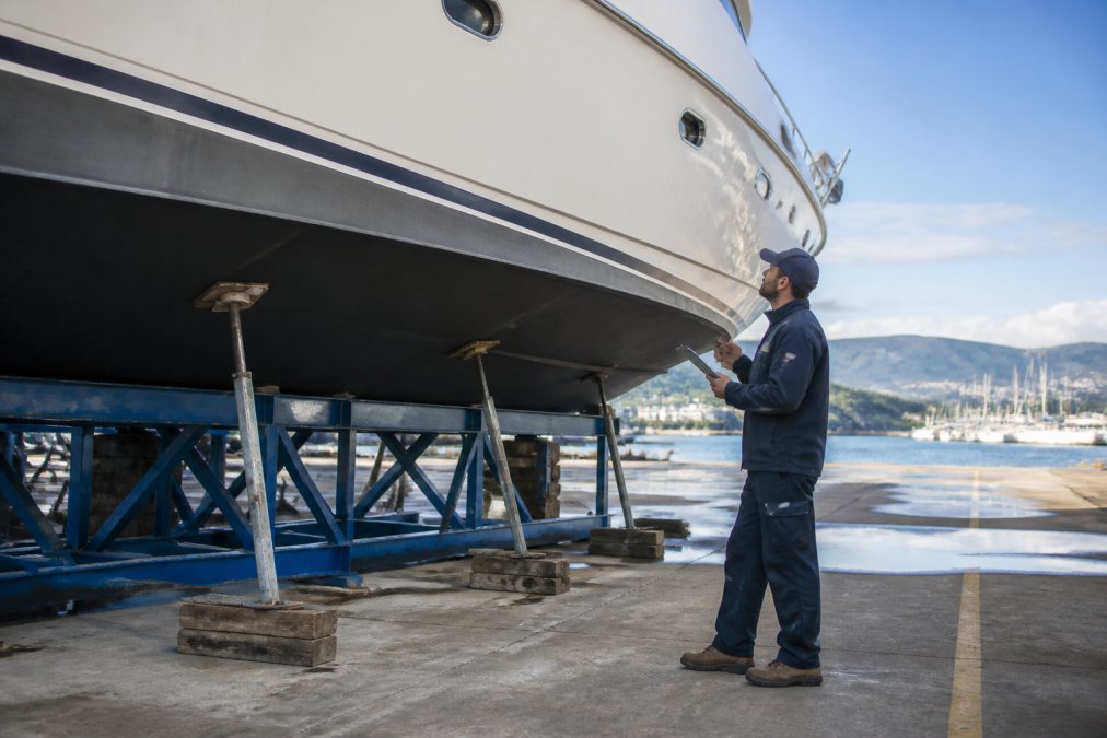Marine surveyor inspecting a white yacht hull with a clipboard before buying a yacht
