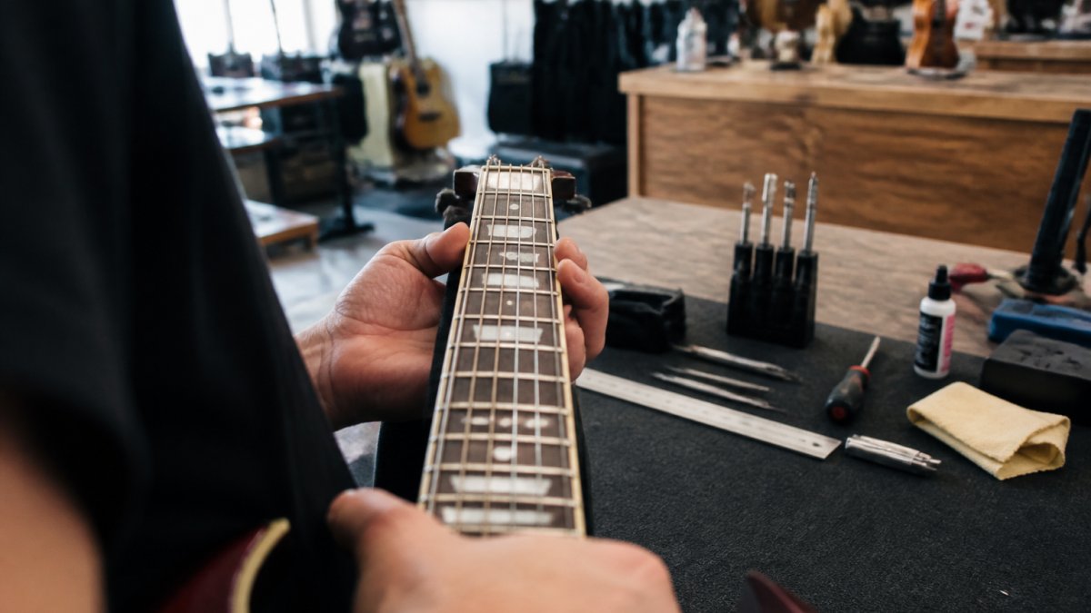 Musician sighting down a guitar neck to check string action and fret straightness while buying guitars