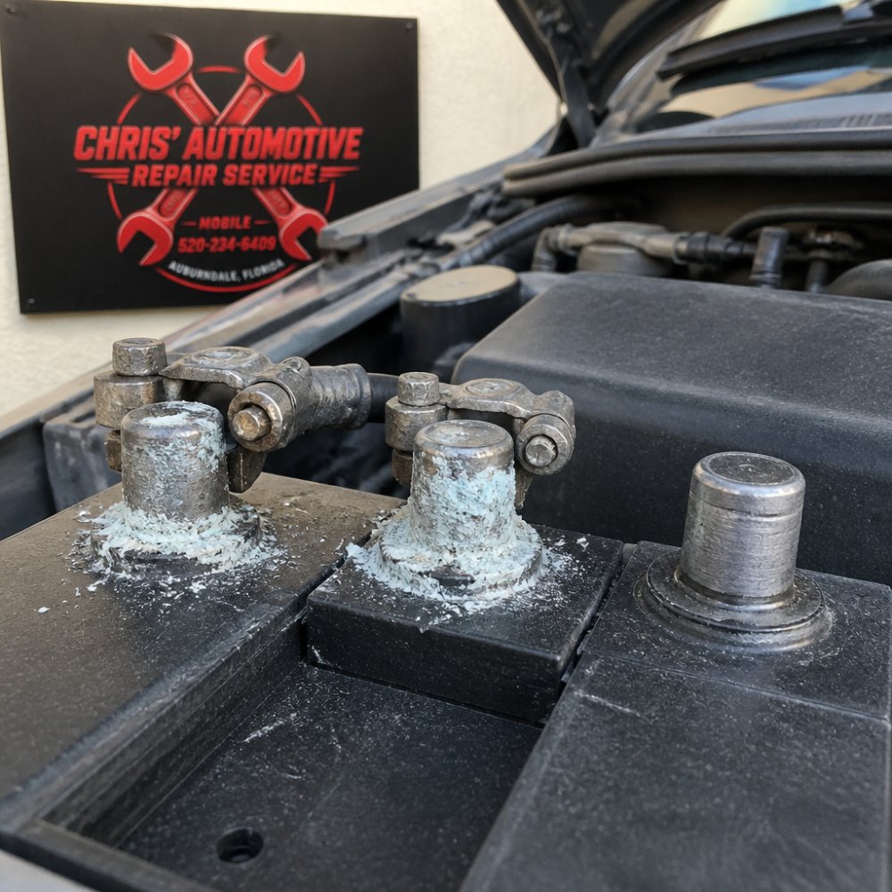 Close-up of car battery terminals showing white corrosion buildup on both positive and negative posts, with a clean battery post visible beside it for comparison