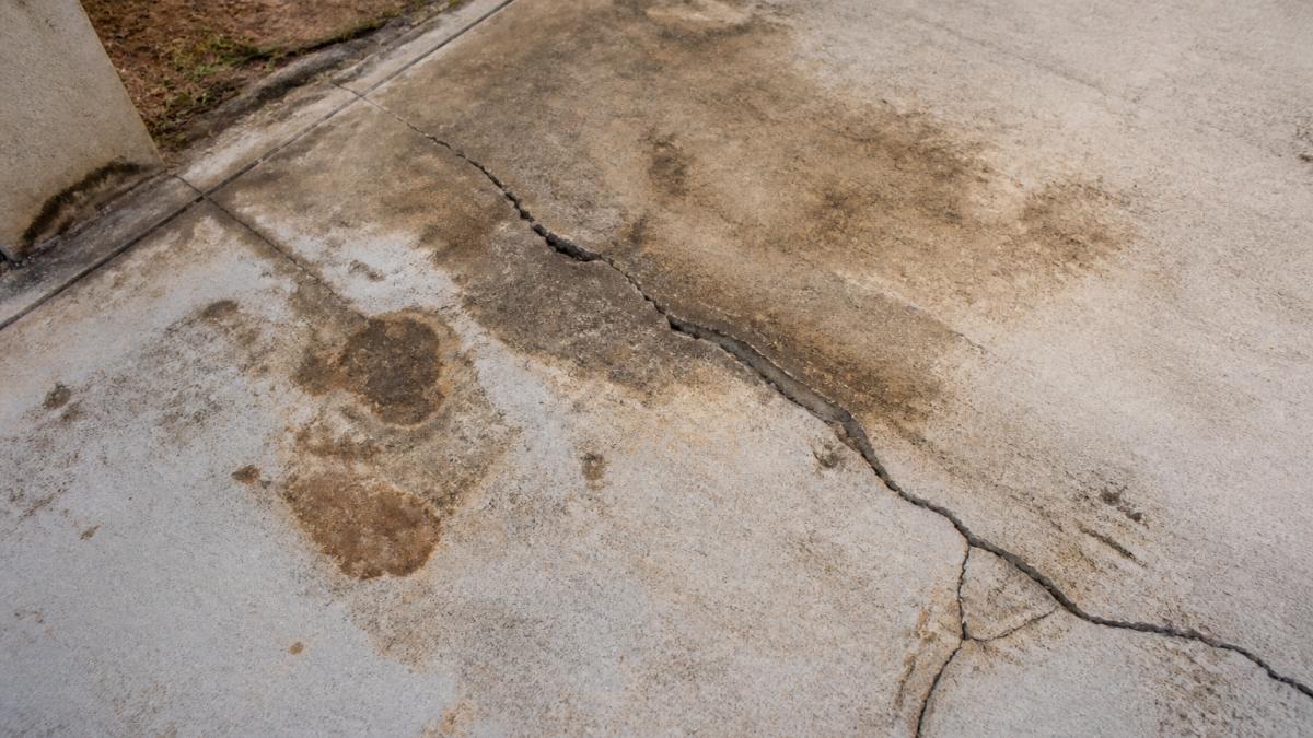 Close-up of weathered concrete patio surface showing visible cracks, spalling edges, and discoloured staining with water damage marks