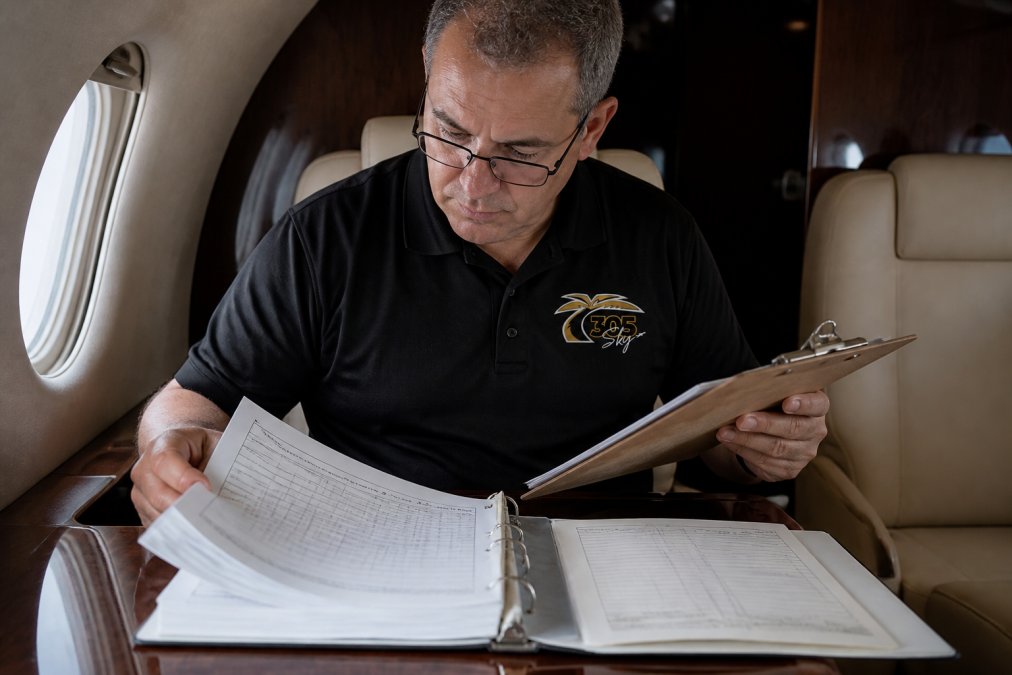 Licensed aircraft inspector reviewing detailed maintenance logbook and inspection documentation in aircraft cabin, clipboard in hand, examining records under cabin lighting