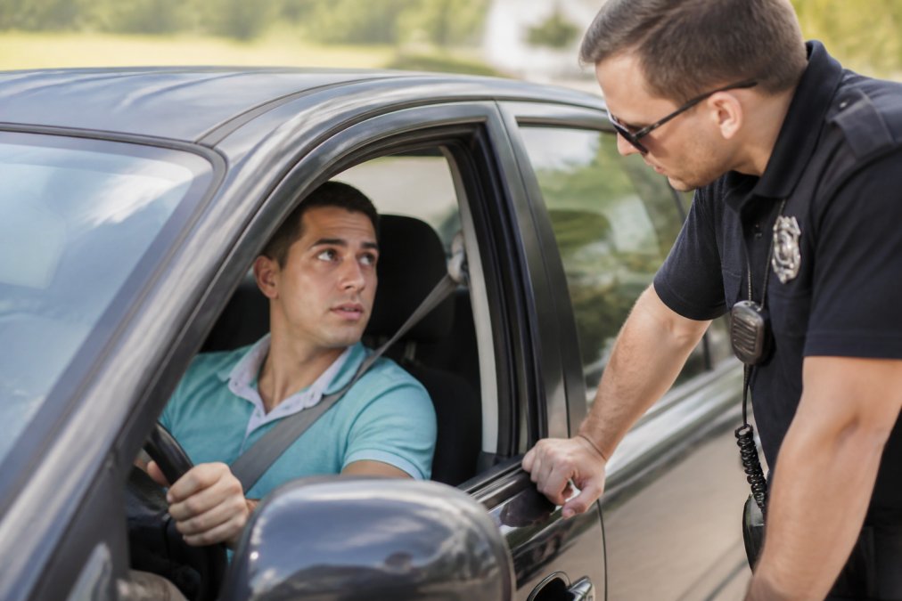 Person speaking respectfully with police officer during traffic stop, hands visible on steering wheel, calm body language and professional interaction