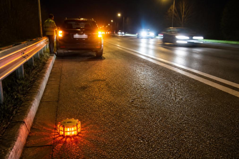 What to Do If Your Car Breaks Down at Night A car pulled onto the hard shoulder at night with hazard lights flashing and a high-visibility warning beacon placed on the road behind it, headlights of passing traffic illuminating the scene
