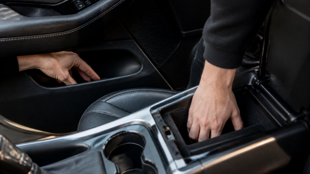 Close-up of hands checking inside a car door pocket and center console, showing typical places where lost key fobs are found