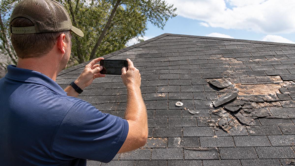 Homeowner using a smartphone to document missing shingles and roof debris after a storm to know what to do if your house is