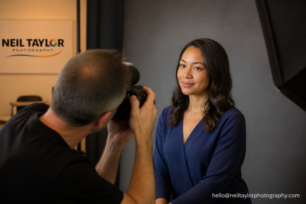 Professional actor in jewel-tone deep blue blouse against neutral grey background, demonstrating how colour complements warm skin tone and creates visual focus for camera