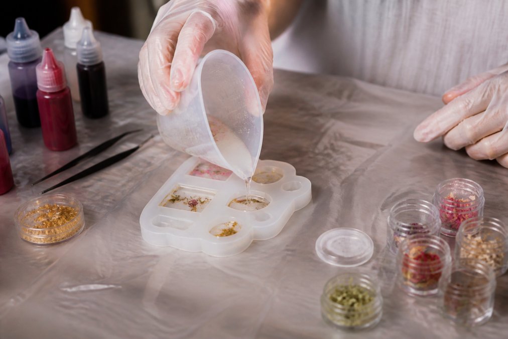 Hands pouring resin from a silicone cup into a jewelry mold to show what tools do i need for resin jewelry.