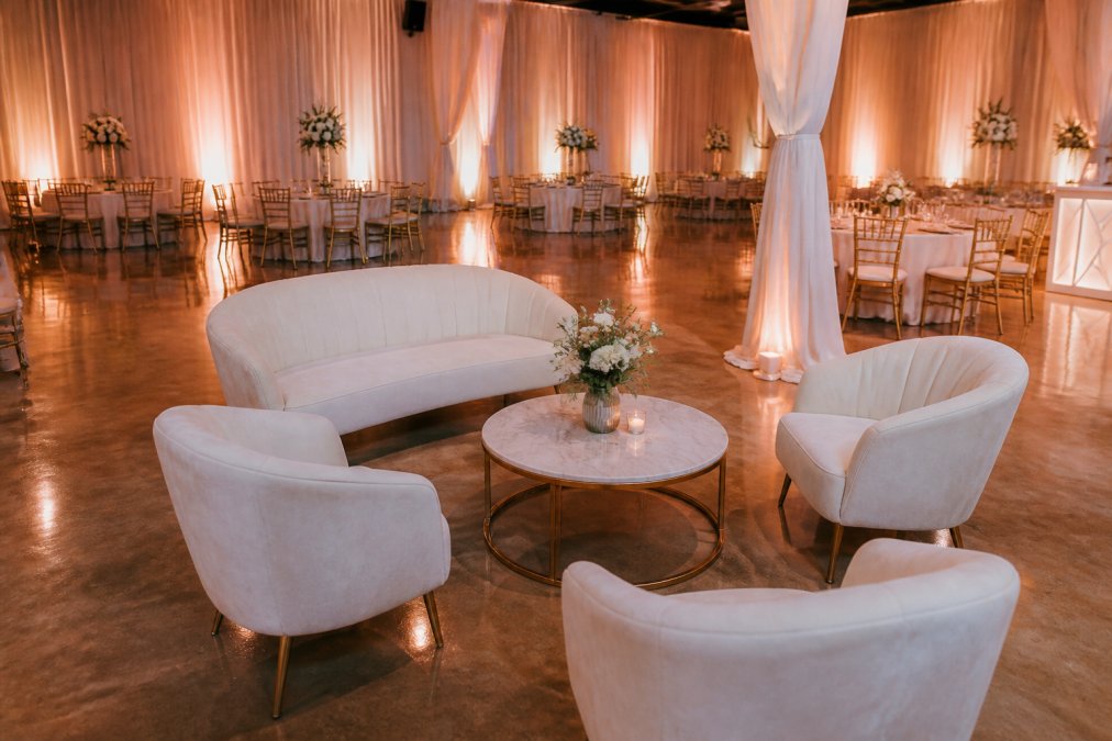 Elegantly decorated venue rental space with intimate lounge seating, warm uplighting, and sophisticated draping.