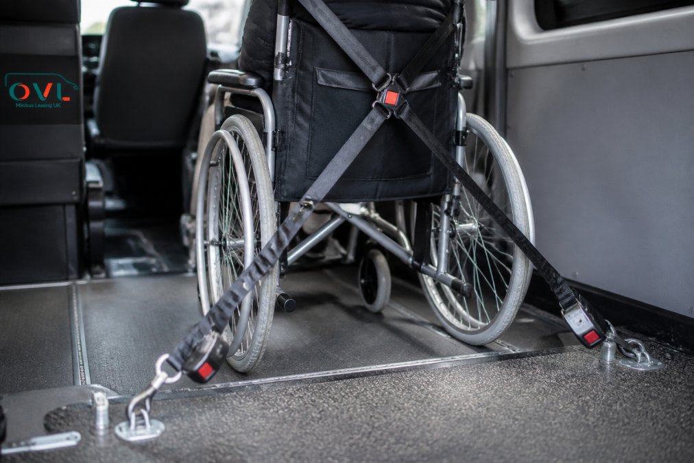 Close-up view of a wheelchair properly secured with restraint straps and tie-down points inside a minibus, showing the correct positioning and attachment method