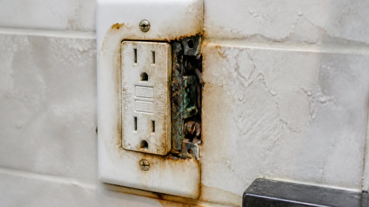 Close-up of a bathroom wall outlet with visible corrosion, water staining, and deteriorated connections showing moisture damage