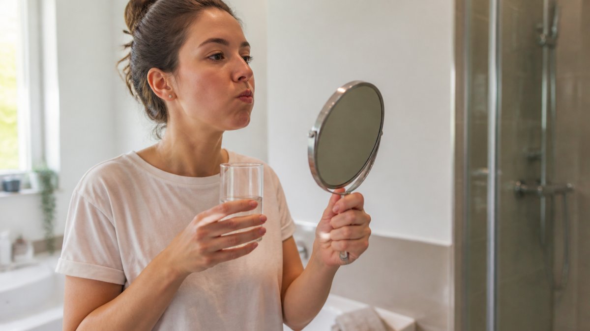 A person gently rinsing their mouth with warm salt water in a bright bathroom, holding a small mirror to check their teeth, looking calm and reassured