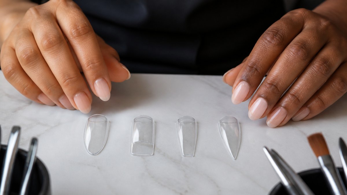 Professional nail technician's hands displaying four different Apres Gel-X tip shapes (almond, square, coffin, stiletto) arranged on a light surface, showing natural and sculpted finishes in various skin tones with natural window lighting