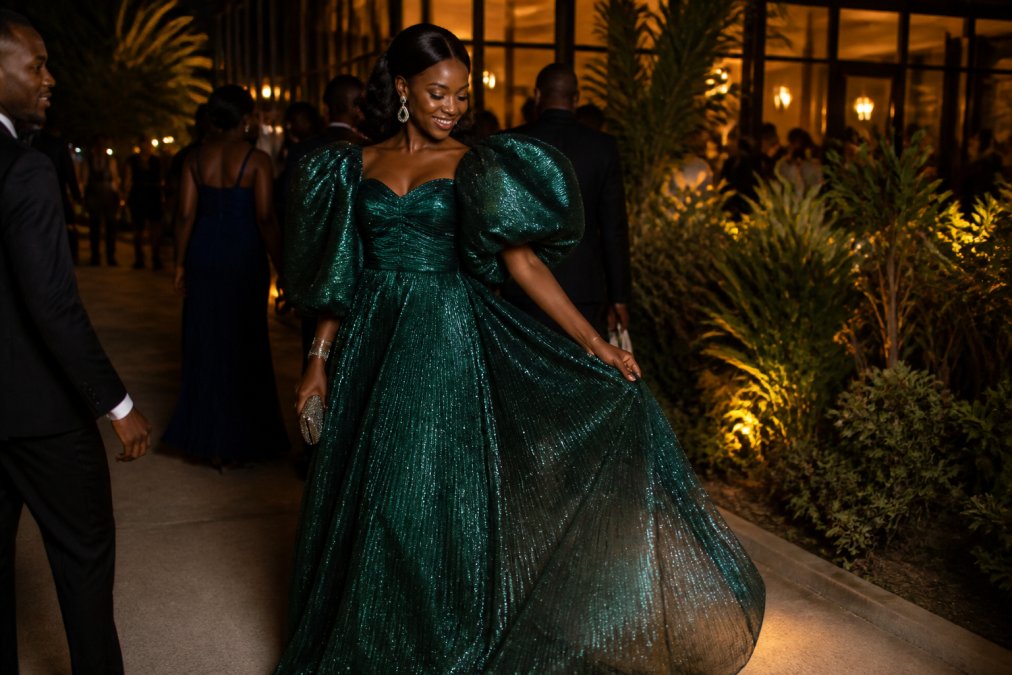 Woman wearing an emerald green metallic shimmer gown with dramatic puff sleeves at a formal evening event, showcasing jewel-like finishes and graceful movement of the fabric under soft lighting