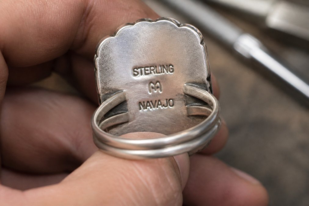 Detailed macro photograph of sterling silver hallmarks and artisan signatures stamped on the back of a handcrafted Navajo ring, showing the clarity and depth of professional silversmith stamps