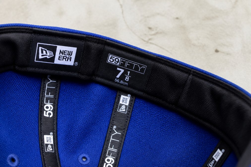 Close-up of the interior sweatband and official licensing tag inside a New Era fitted baseball cap, showing clear embroidered branding, stitching quality, and size markings under bright natural light