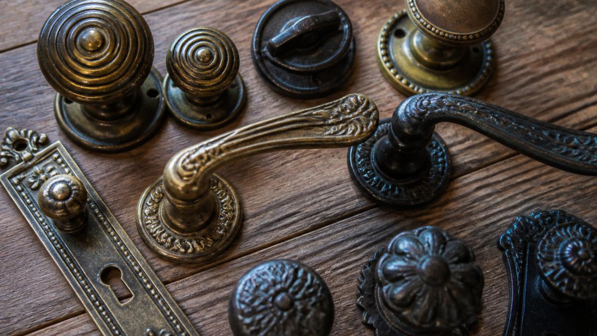 Close-up of a collection of authentic brass and cast iron Victorian door handles and knobs displayed on a wooden surface, showing varied period finishes including tarnished brass, aged bronze, and blackened cast iron with ornate Victorian designs