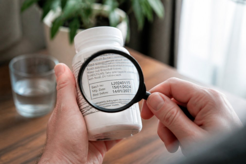 Person holding a supplement bottle and examining the batch number label with a magnifying glass, showing the traceability information on the packaging