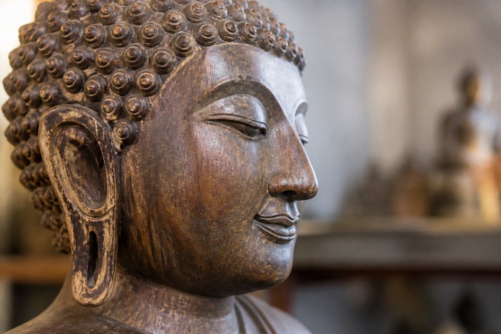 Close-up of hand-carved wooden Buddha statue showing detailed tool marks, natural patina, and intricate facial features carved by artisan hands