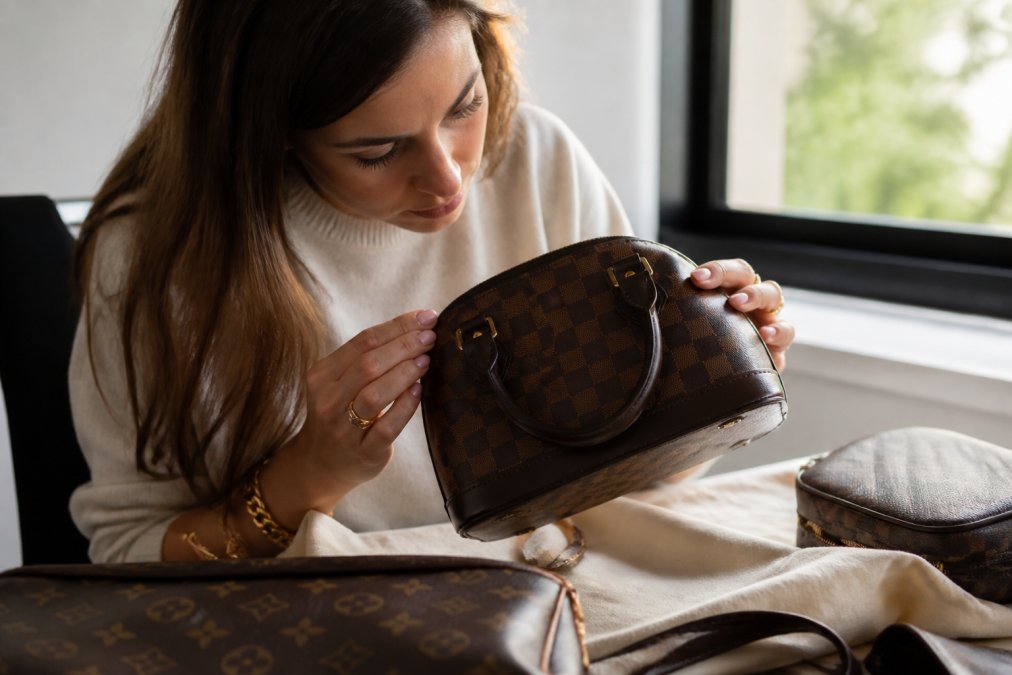 Woman carefully examining a luxury designer handbag, inspecting the stitching, hardware details, and serial numbers in natural daylight near a window