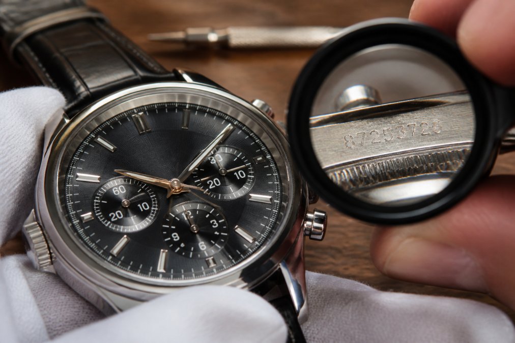 Close-up of a luxury watch face showing detail of dial, hands, and serial number engraving on the caseback under magnification