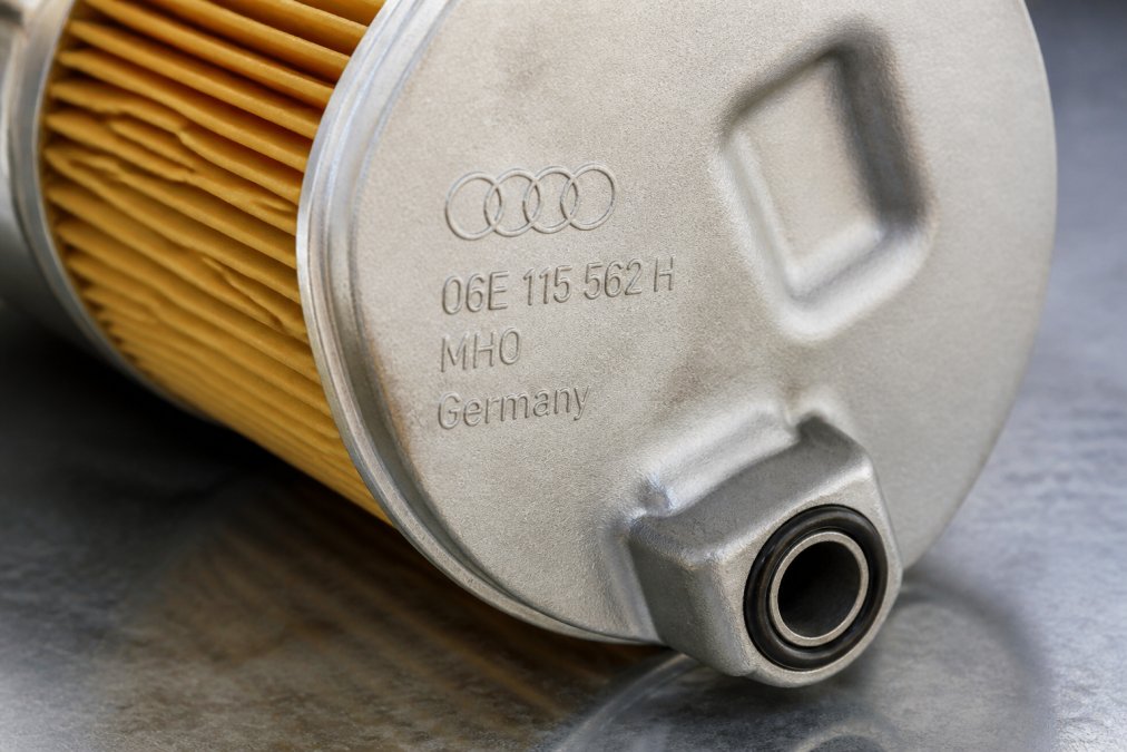 Close-up of genuine OEM Audi filter showing crisp part number stamping, Audi logo embossment, and intact gasket seal on aluminum housing under bright lighting