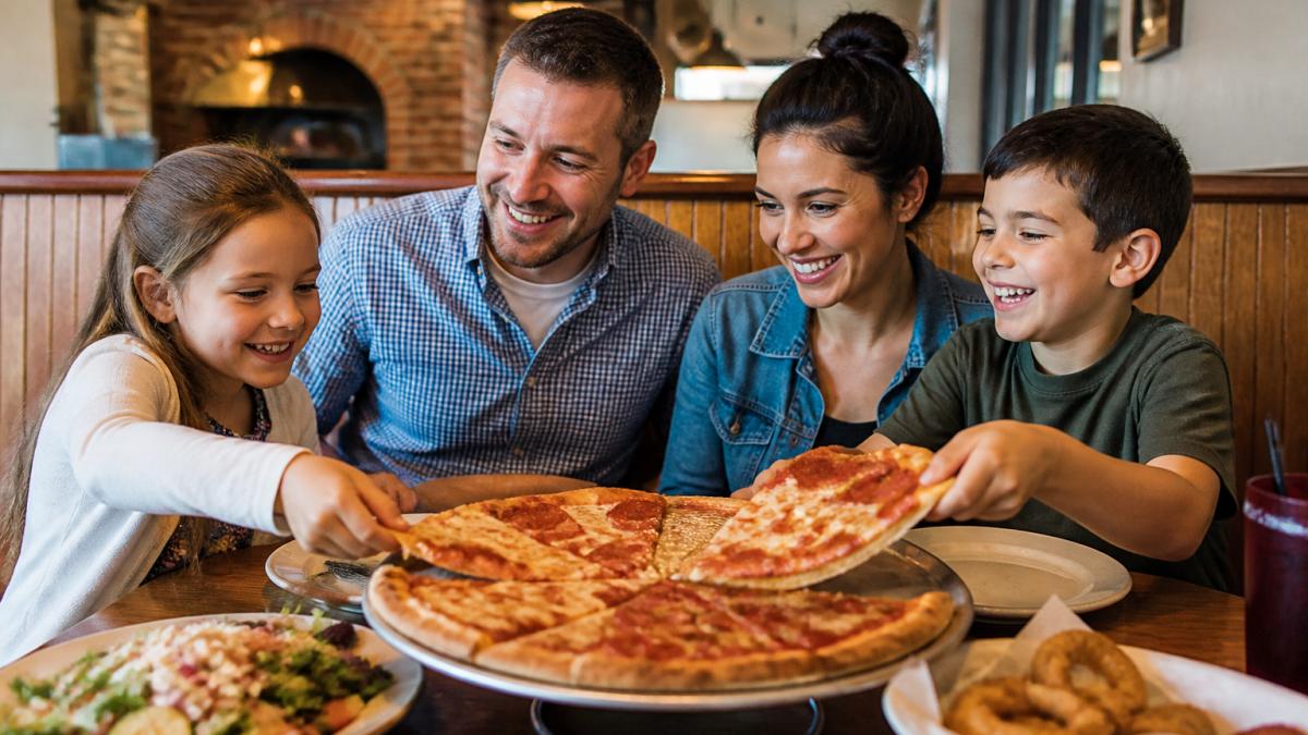 Family with two children seated at a restaurant table, smiling while enjoying pizza and casual meal together in a warm, welcoming dining room with soft lighting