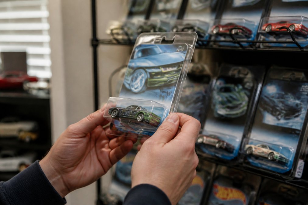 A collector's hands holding a rare Hot Wheels AcceleRacers diecast car in its original carded packaging, with other carded models and a display shelf blurred in the background