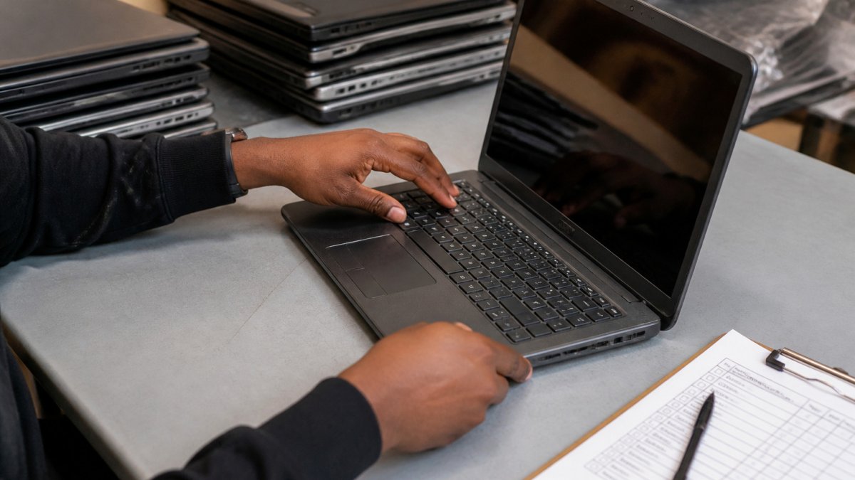 Hands inspecting a government surplus electronics laptop using a printed condition checklist on a desk