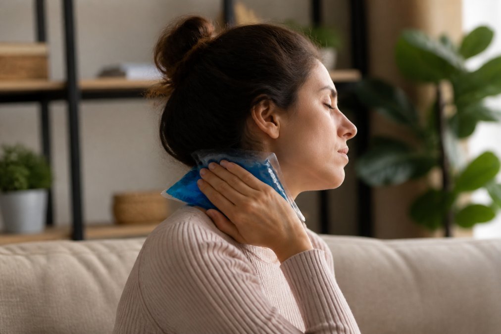 Person sitting on a couch applying an ice pack to their neck after an accident, with calm supportive environment and natural lighting in the background
