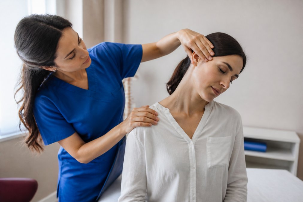 Healthcare provider performing cervical spine examination on patient in clinical setting, with focus on range-of-motion assessment and palpation technique under bright office lighting