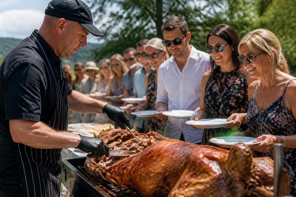 Professional chef carving freshly roasted whole hog at outdoor event with guests gathered around carving station, golden-brown meat being sliced onto white plates under afternoon sunlight