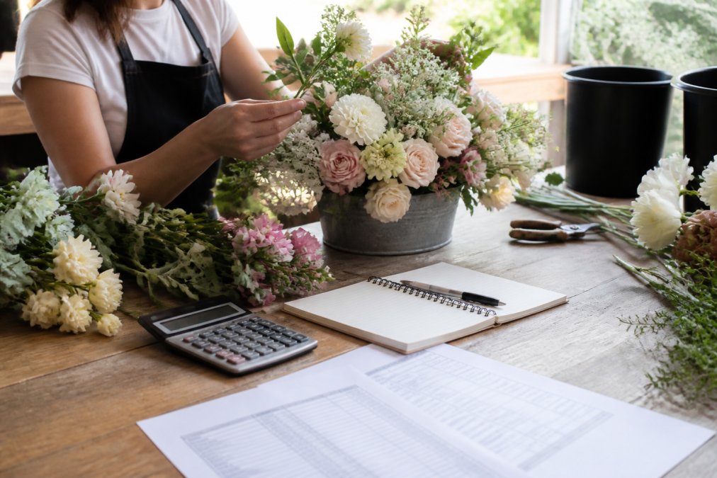Hands arranging fresh flowers in a wedding bucket design, carefully selecting blooms for a custom color palette in soft natural light