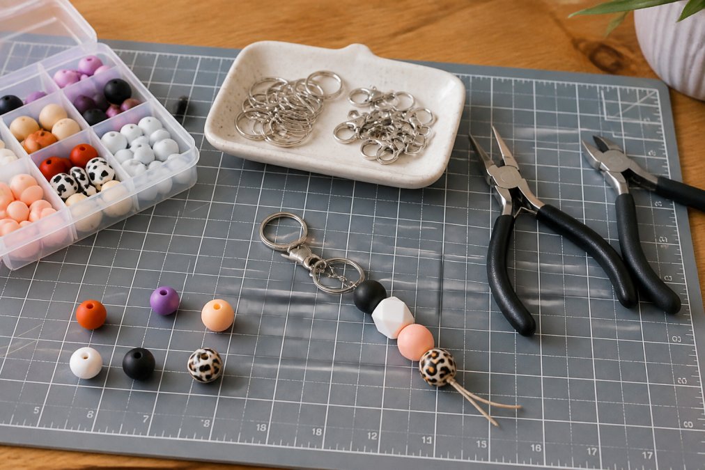 Jewelry pliers and wholesale keychain hardware displayed on a workbench with colorful silicone beads.