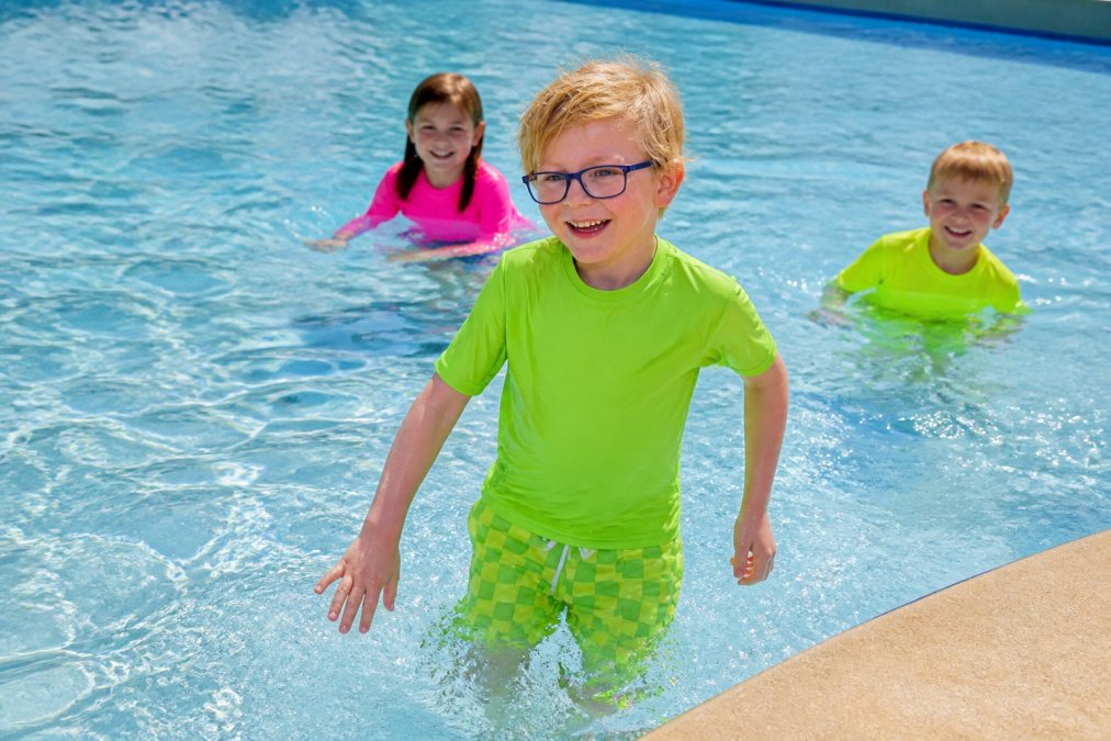 Young swimmers wearing bright neon high-visibility swimsuits in a clear swimming pool, with the vibrant colors contrasting sharply against the blue water and pool deck